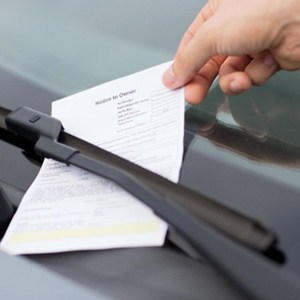 A person is picking up a parking ticket against a car windshield.